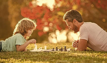 happy family of father man and son kid playing chess on green grass in park outdoor, fatherhood