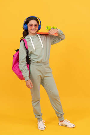 Happy teenager in activewear holding pennyboard yellow background, board skatingの写真素材