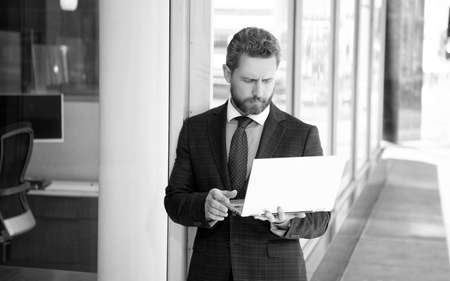 serious bearded mature man freelancer in suit chatting on laptop at business office, online chat