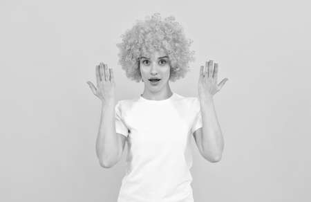 surprised freaky woman in curly clown wig with raised hands, surprise