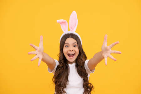 happy amazed kid in bunny ears reach hands on yellow background, easterの写真素材