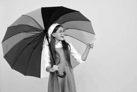 happy school girl in glasses. teen child under colorful parasol pointing finegr.の写真素材