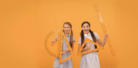 Happy teen girls hold geometric tools for geometry lesson orange background copy space, schoolの写真素材