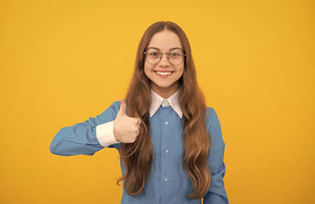 Happy nerdy-looking girl child give thumbs up satisfaction hand gesture yellow background, childhood