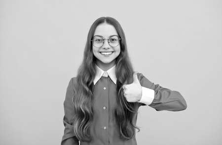 Happy nerdy-looking girl child give thumbs up satisfaction hand gesture yellow background, childhood