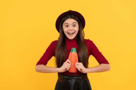amazed girl in hat hold shampoo. presenting cosmetic product for teen.
