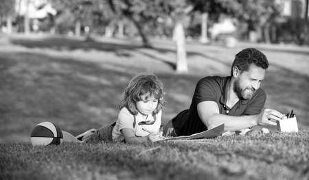 happy family day. dad and kid boy relax on grass in park. child hold learning to draw.の写真素材