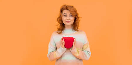 glad redhead woman with red heart on orange background with copy space. valentinesの写真素材