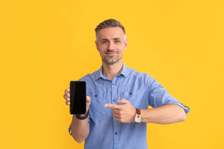 smiling man pointing finger on phone on yellow background, copy space, presentationの写真素材