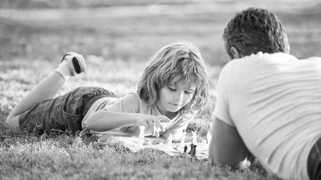 happy family of dad and son child playing chess on green grass in park outdoor, tactic