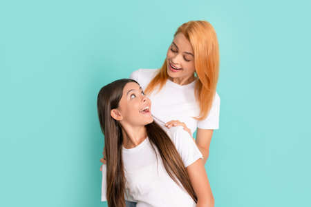 friendly family of mother and daughter girl in white shirts on blue background, motherhood