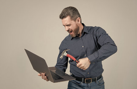 Angry man hit laptop computer with hammer grey background, crash