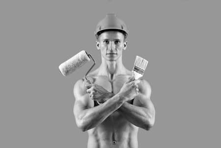 Sexy man with muscular torso hold paintroller and paintbrush for decorating and painting, painterの写真素材