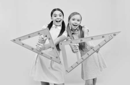 Happy school age kids hold triangular rulers yellow background, geometry