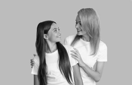 loving smiling woman hug daughter in white shirts on blue background, friendship