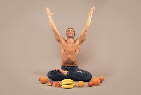 Athletic man sit in lotus position with raised hands and natural organic fruit, yoga nutrition.の写真素材
