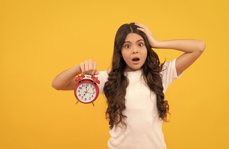 worried teen girl hold retro alarm clock showing time, late awakeningの写真素材