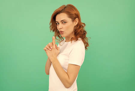 serious confident redhead girl with curly hair with gun gesture on blue background, confidenceの写真素材