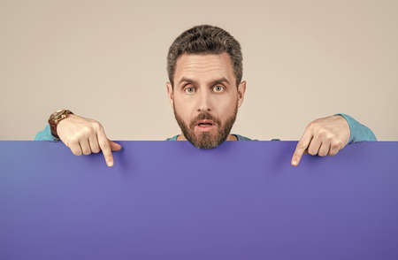 surprised bearded man pointing finger on blank blue paper banner with copy space for ad, gossip.の写真素材