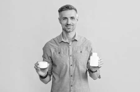 smiling adult guy holding drug jar and cream on yellow background, daily habits