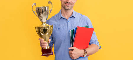 smiling man hold champion cup and notebook on yellow background, award