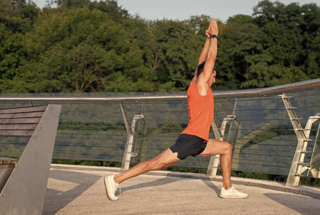 Fit man hold virabhadrasana pose doing crescent lunge stretch on promenade, yogaの写真素材