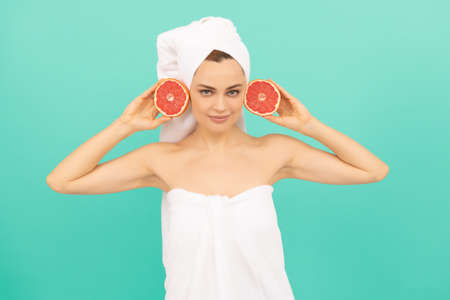 young woman in towel after shower with grapefruit on blue background. vitamin c