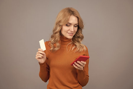 Girl pay with bank card on smart phone grey background copy space, mobile banking