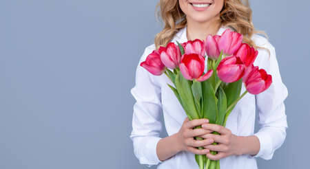 positive blond woman with spring tulip flowers on grey background