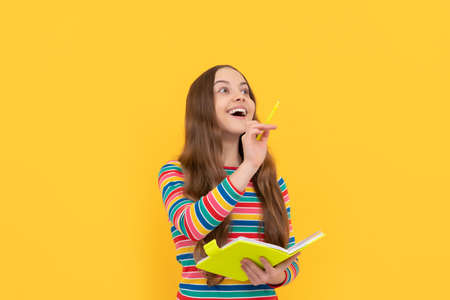 Happy kid genius got inspiration holding book and pointing pen up yellow background, idea