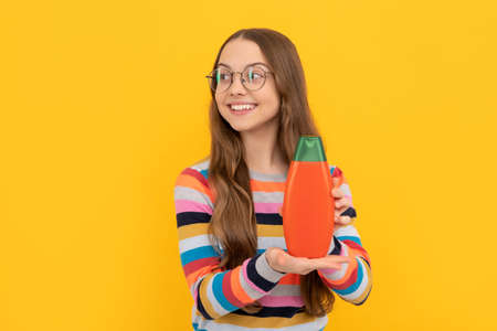 cheerful child long hair in glasses showing shower gel bottle, advertising