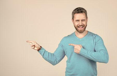 happy mature man with beard pointing finger on grey background with copy space, advertising