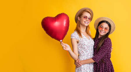 smiling mom and daughter hold love heart balloon on yellow backgroundの写真素材