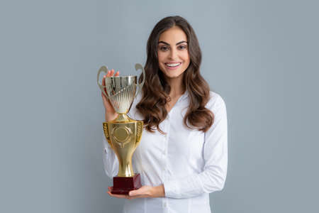 Cheerful businesswoman holding trophy standing posing on grey background.