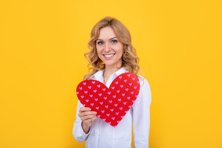 smiling woman with red love heart on yellow backgroundの写真素材