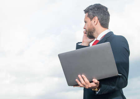 businessperson in suit speaking on phone and hold laptopの写真素材