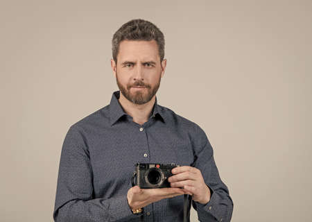 Bearded man in casual style shirt hold rangefinder photo camera on hand grey background, photography
