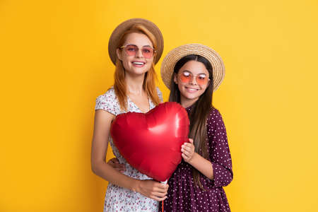 smiling mother and daughter holding love heart balloon on yellow backgroundの写真素材