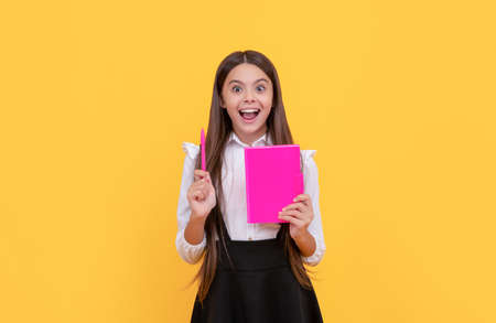 Happy child genius hold school book pointing pen up yellow background, ideaの写真素材