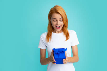 Happy birthday. Woman holding gift box with ribbon. Expressive facial expressions with suprised face. Studio portrait over blue background.の写真素材