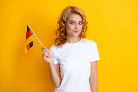 Portrait of positive student woman holding German flag. Isolated on yellow background. Happy girl holding flag of Germany, immigration and travelling in Europe. Deutschland, deutsche flag.の写真素材
