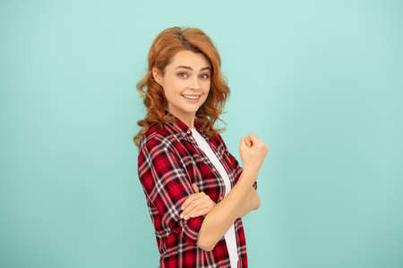 happy redhead woman in checkered shirt threatening with fist on blue background