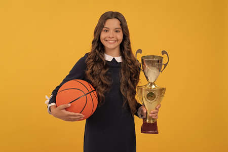 cheerful kid hold basketball ball and champion cup on yellow background, sport successの写真素材