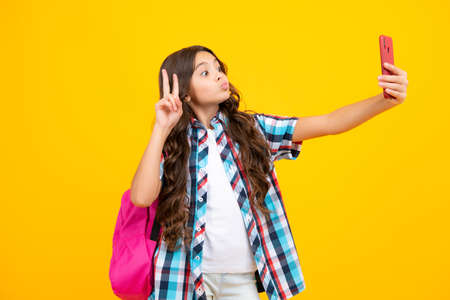 Funny face. Portrait of school girl holding phone, isolated on yellow background.の写真素材
