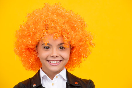 Teenage girl with yellow wig. Funny child wearing orange curly wig hair. Happy girl face, positive and smiling emotions.の写真素材