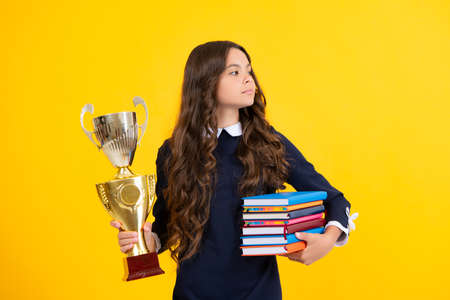 Schoolgirl in school uniform celebrating victory with trophy. Teen holding winning prize on yellow background. School kid win gold trophy.の写真素材