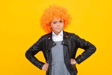 Funny kid with curly hair wig. Cute little girl with fancy hair. Child wearing bright redhead clown hair wig. Angry teenager girl, upset and unhappy negative emotion.の写真素材