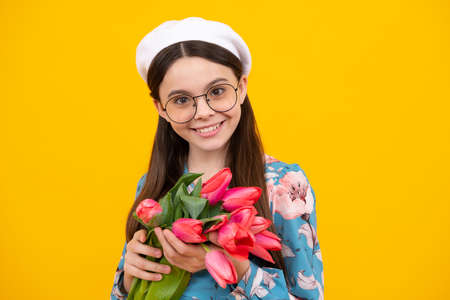 Happy teenager girl in beret hat hold spring tulip flowers on yellow background. Child with spring...