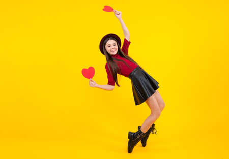 Cheerful lovely romantic teen girl hold red heart symbol of love for valentines day isolated on yellow background. Excited teenager, glad amazed and overjoyed emotions.の写真素材