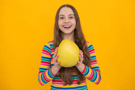 Summer fruits. Teenager child girl hold citrus fruit pummelo or pomelo, isolated on yellow background. Kid healthy eating.の写真素材